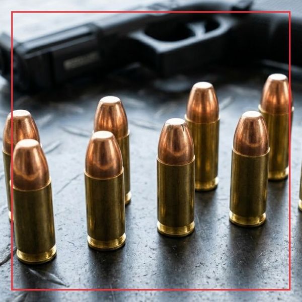 A close-up square photograph highlighting several polished brass centerfire handgun cartridges standing upright on a dark, textured metal surface.