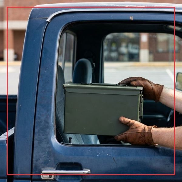 A close-up square photograph of a generic green ammo can being stabilized by gloved hands inside a pickup truck, illustrating a successful local logistics pickup.