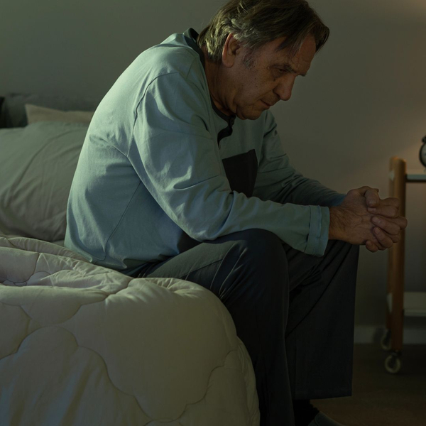 older man hunched over the side of his bed