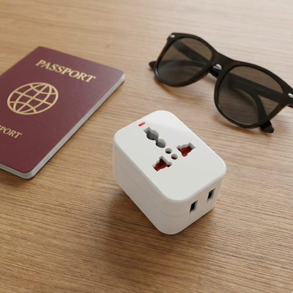 A flat lay of travel essentials including a passport, sunglasses, and a universal power adapter.