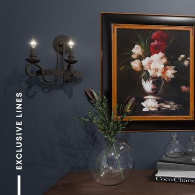 A wall sconce illuminates a framed painting of flowers next to a vase of greenery. A wall sconce illuminates a framed painting of flowers next to a vase of greenery.
