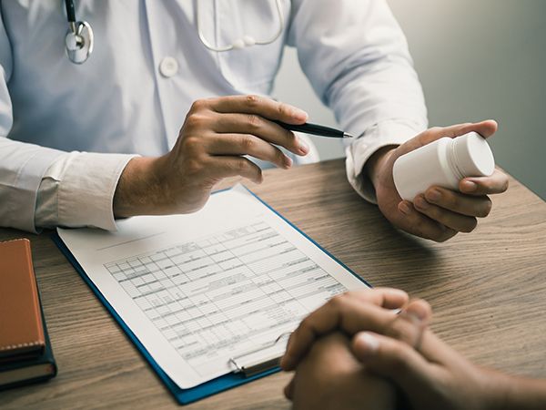 a doctor holding a bottle and talking with a client in front of a chart