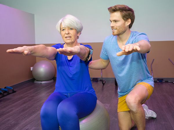 an older woman practicing her balance on an exercise ball with an instructor
