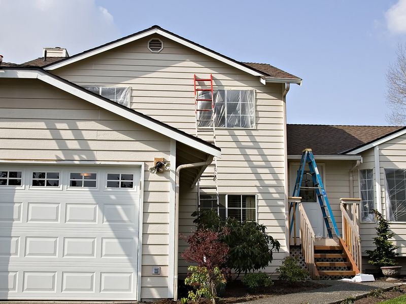 The exterior of a home with the windows covered in plastic and ladders set up around the home. 