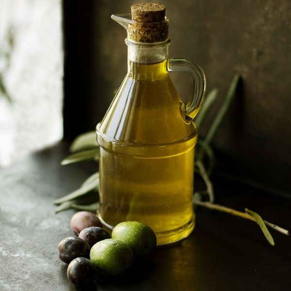 An image of a bottle of olive oil next to some olives.