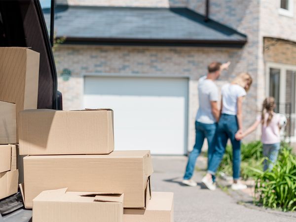 moving boxes stacked next to vehicle, with a family in the background